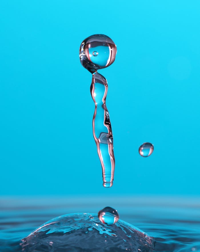 programs-02 A high-speed close-up of a water droplet suspended mid-air on a blue background.